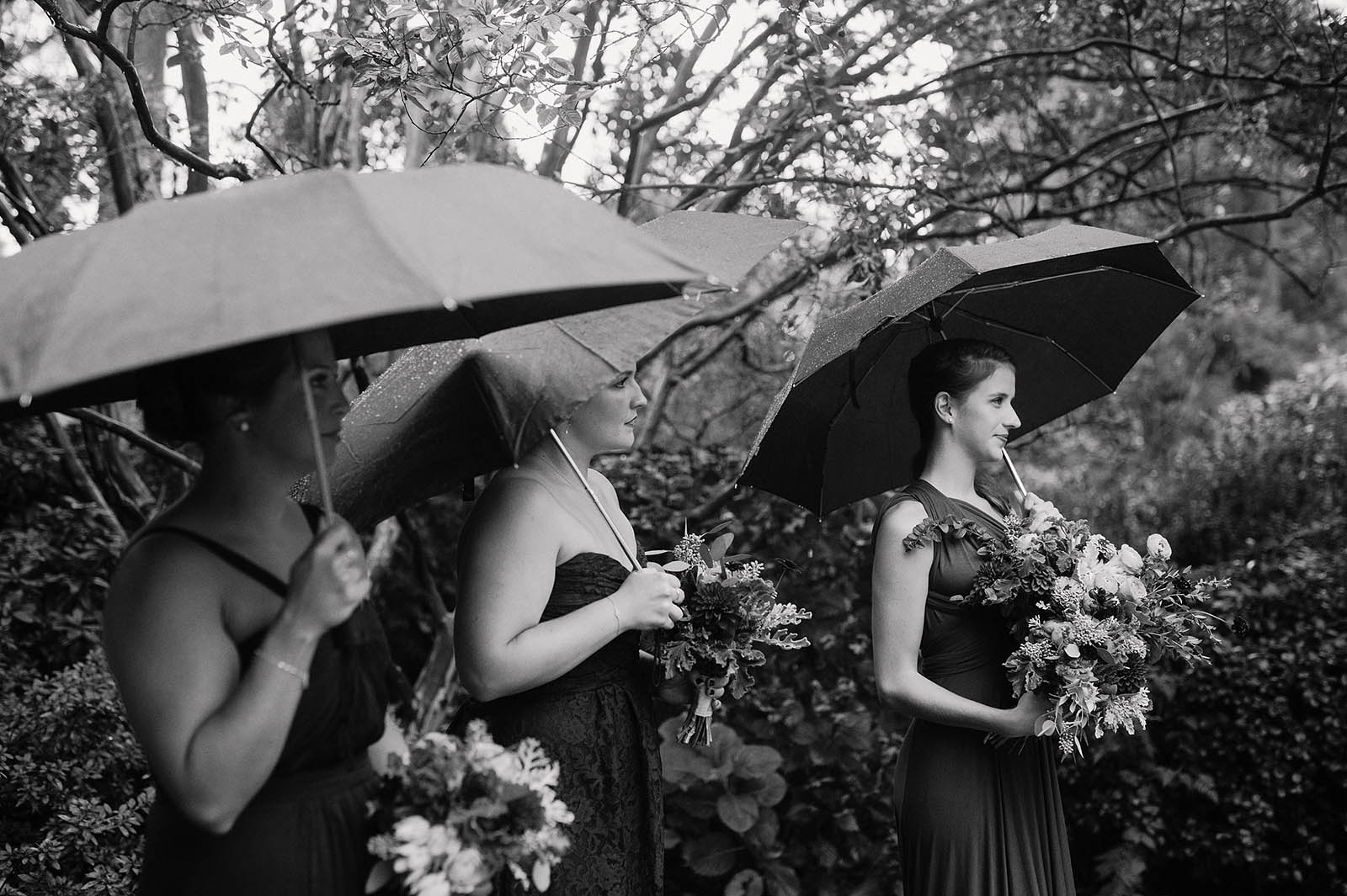 Bridesmaids with umbrellas at a rainy Crystal Springs Rhododendron Garden wedding ceremony