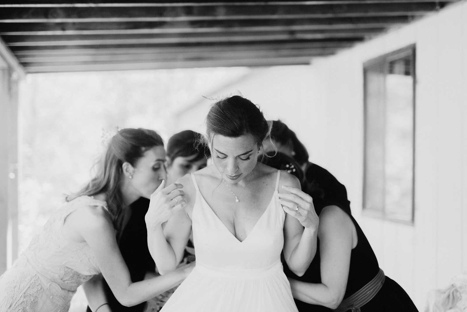 Black and white portrait of bride looking down while her friends tie her dress - Columbia Gorge River Wedding in Oregon