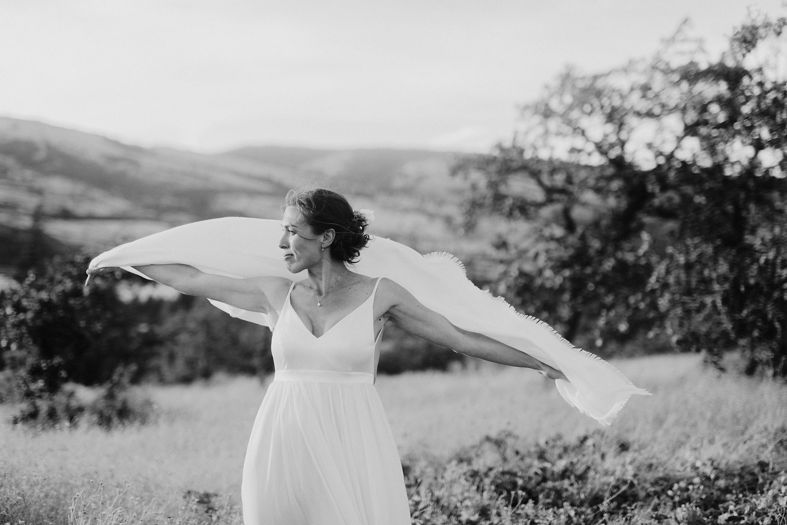 Black and white portrait of bride dancing with her scarf in the wind at a Columbia Gorge River Wedding in Oregon