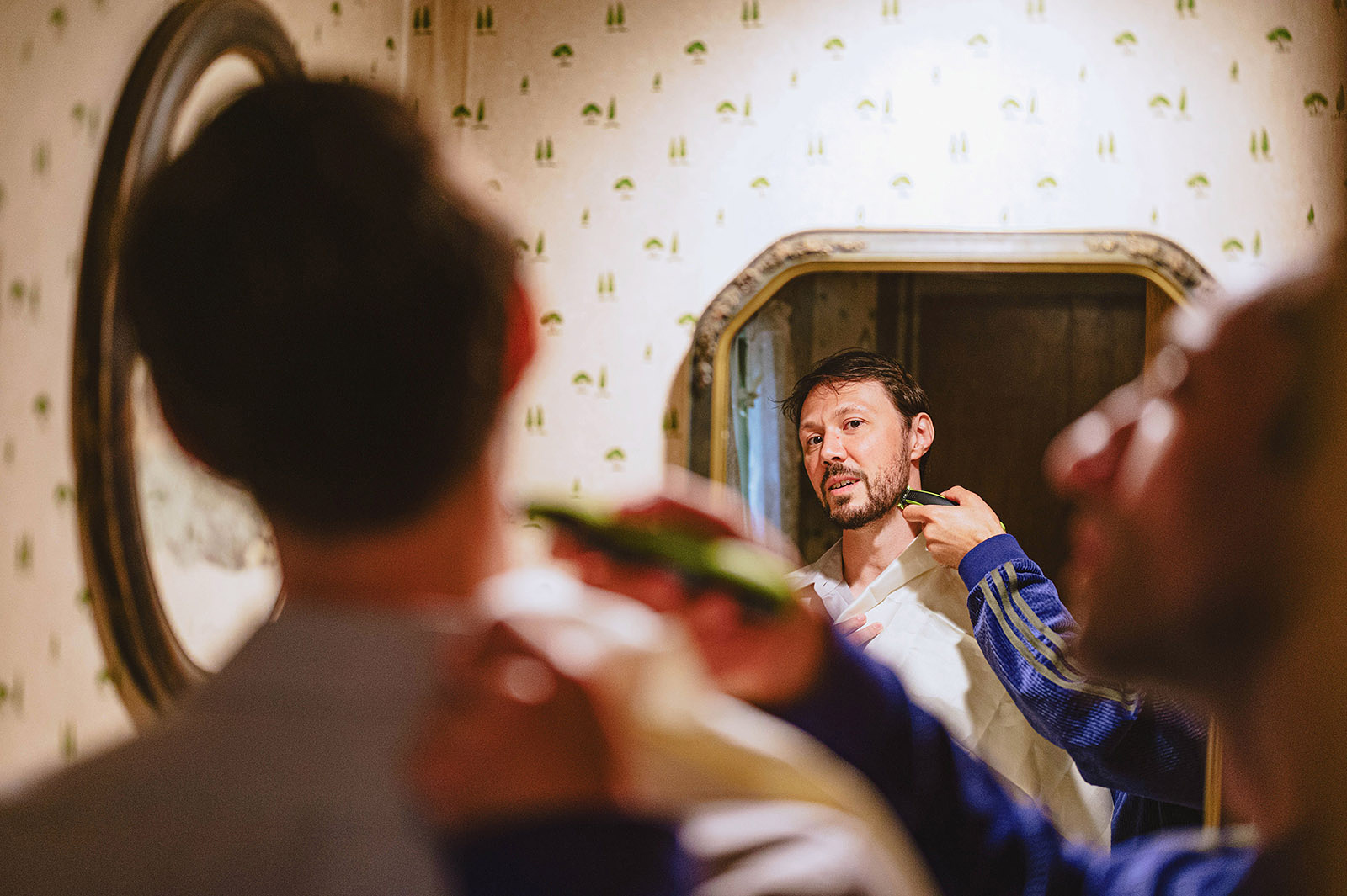 Groom looking in the mirror while a friend touches up his neck shave at Kelly's Trout Creek Inn, WA
