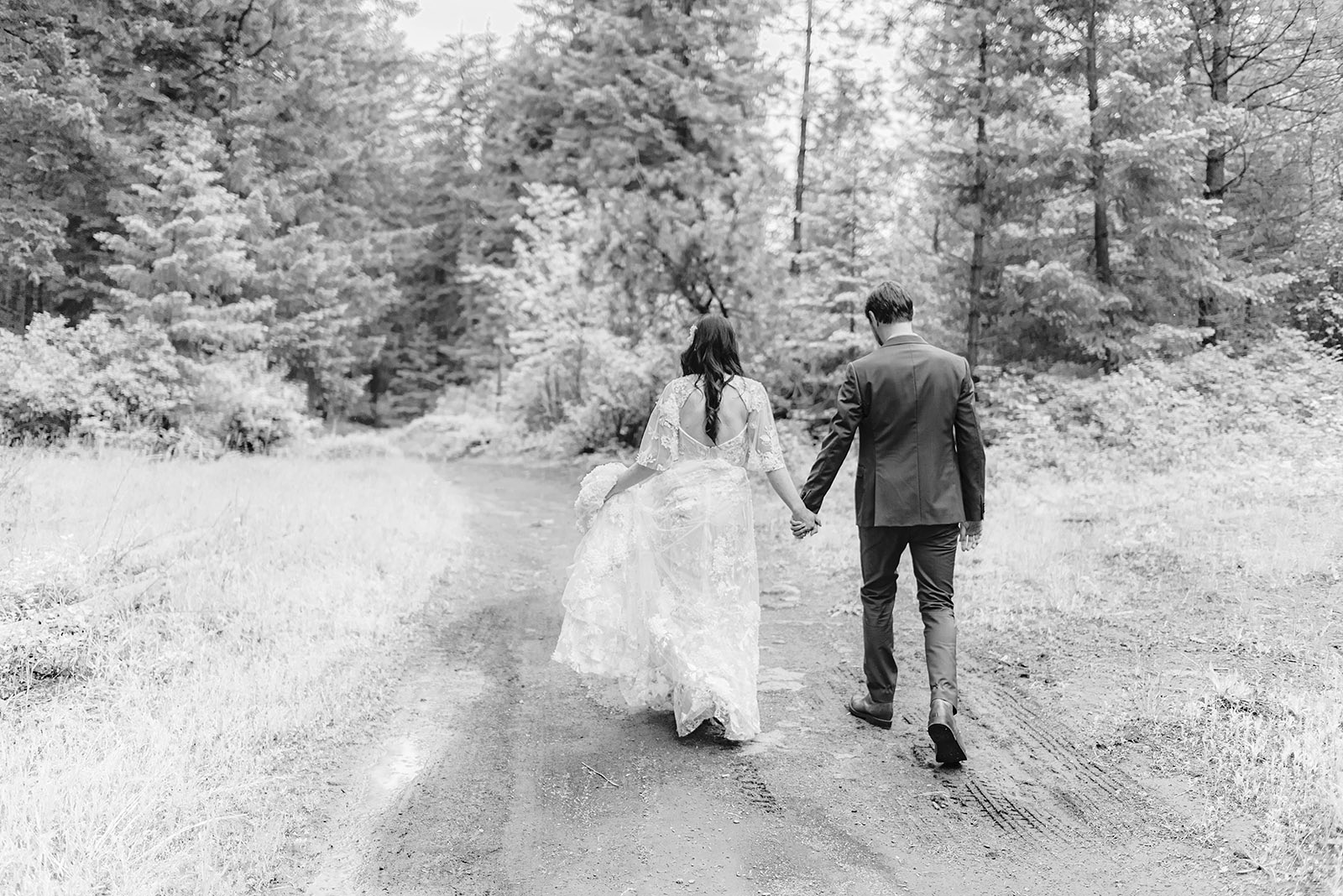 Black and white photo of bride and groom holding hands while walking down a dirt path - Trout Lake Wedding, WA