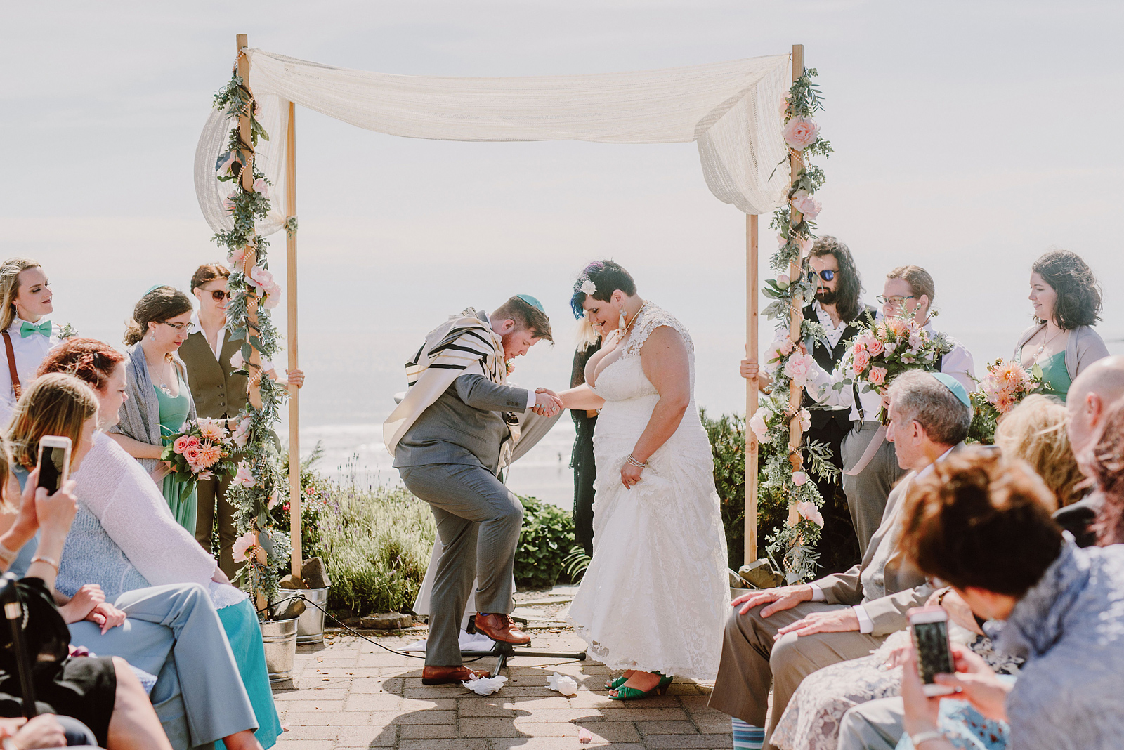 Groom smashing the ceremonial glass at a Jewish wedding - Oceanside Community Club Wedding on the Oregon Coast” title=