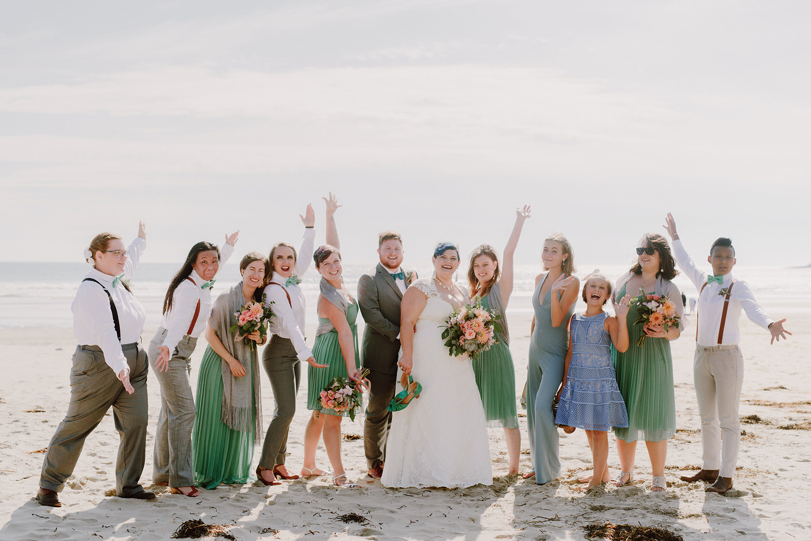 Group photo on the beach of the bride and groom with their spunky wedding party - Oceanside Community Club Wedding on the Oregon Coast” title=