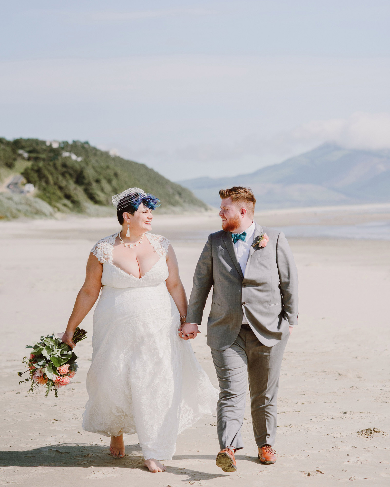 Bride and Groom looking at each other while walking down the beach - Oceanside Community Club Wedding on the Oregon Coast” title=