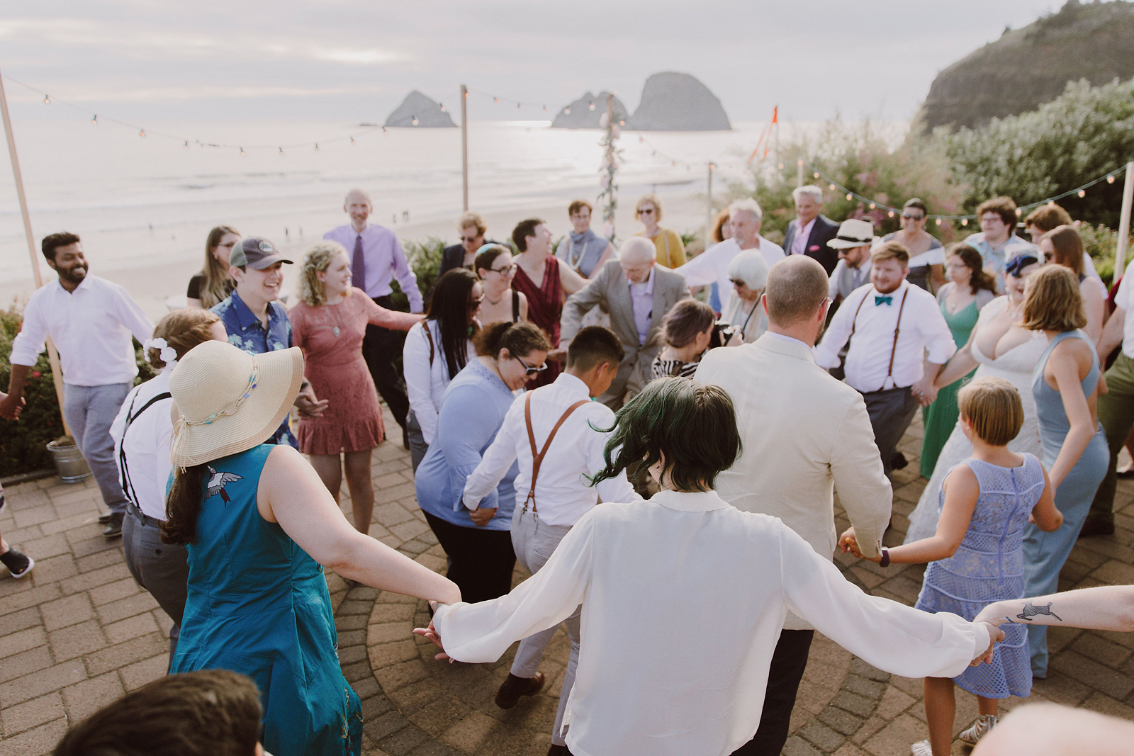 Guests dancing in circles during the hora - Oceanside Community Club Wedding on the Oregon Coast” title=